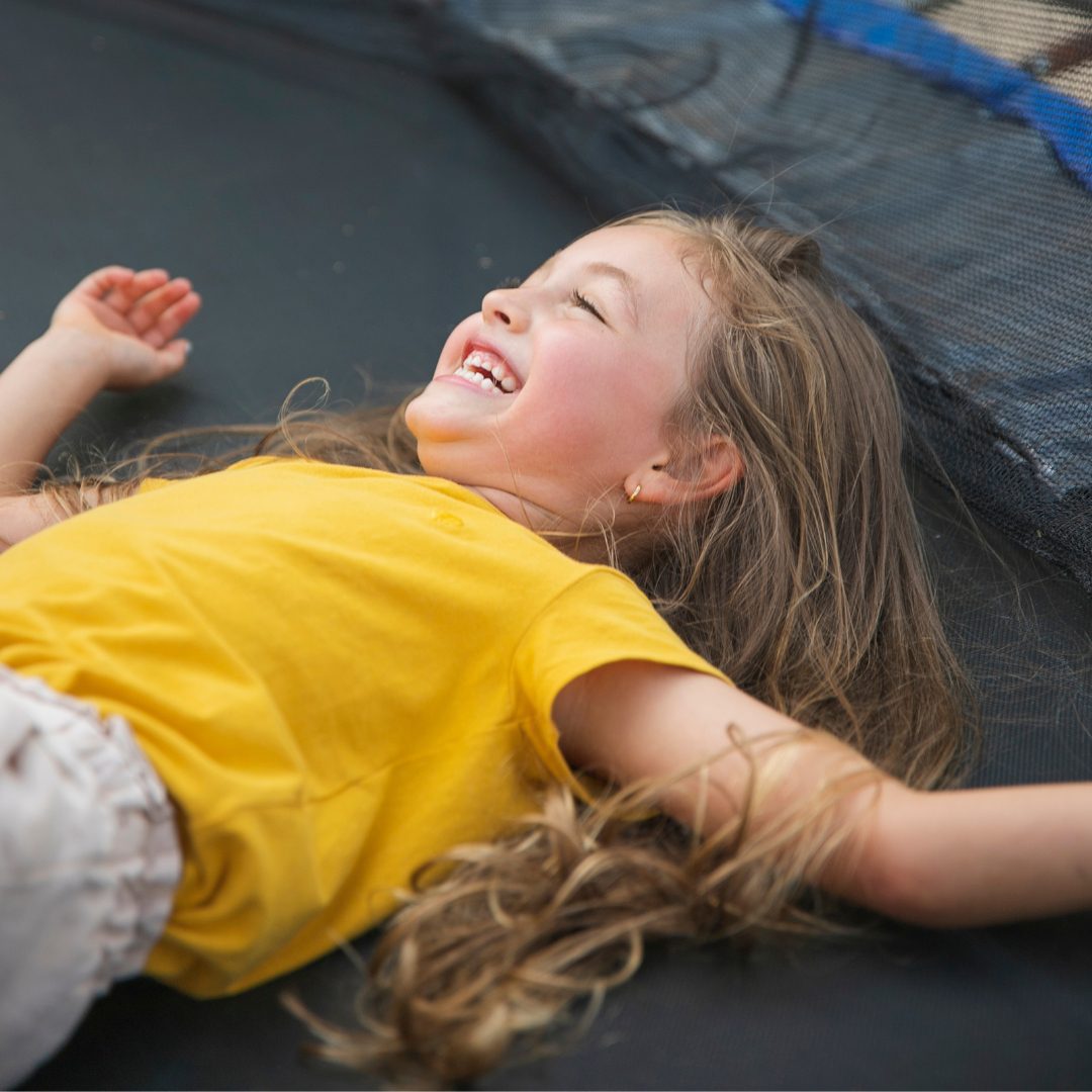 Young girl laughing and laying on a trampoline