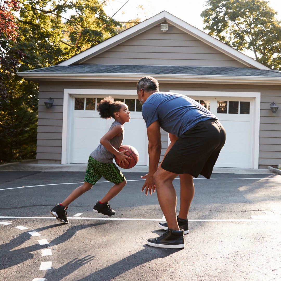 Dad and daughter playing basketball in their driveway