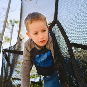 boy crawls under trampoline safety net