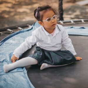 girl wearing glasses rests on side of trampoline 