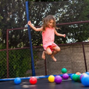 girl jumps above trampoline surface with colorful balls 